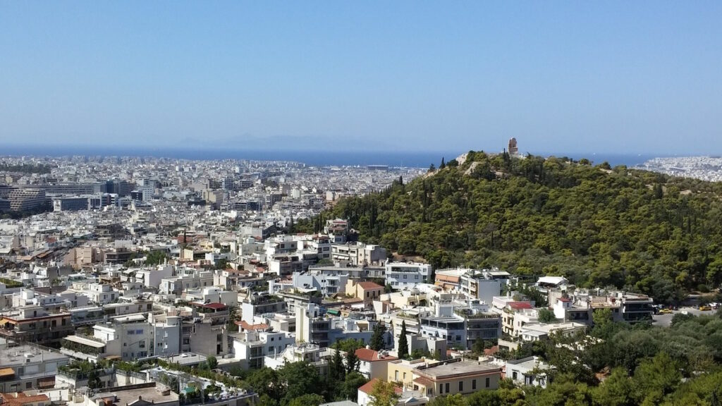City skyline of Athens Greece with urban buildings and green hills overlooking the Mediterranean.