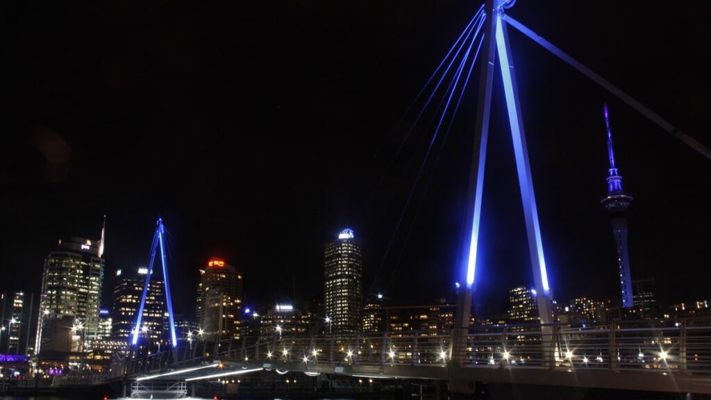 Auckland skyline at night with Sky Tower and illuminated bridge in New Zealand.