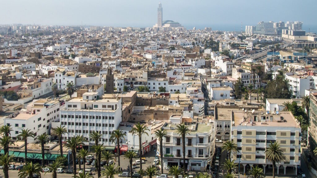 Skyline of Casablanca, Morocco with palm-lined streets and the Hassan II Mosque in the distance.