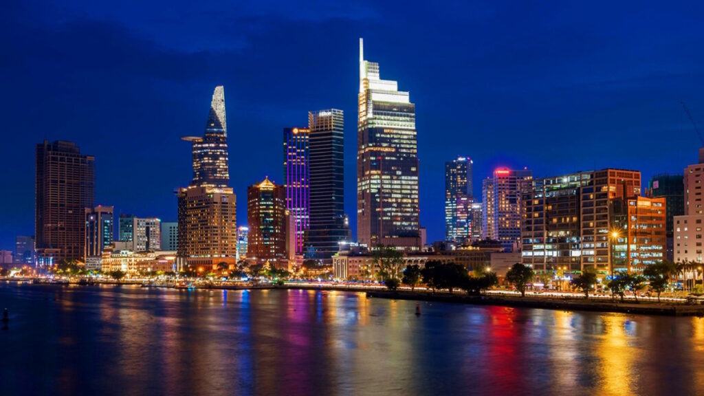 Ho Chi Minh City skyline at night with illuminated buildings and river in Vietnam.