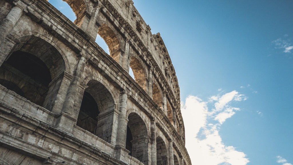 Close up view of the ancient stone arches of the Roman Colosseum against a blue sky on a scenic tour of Italy.
